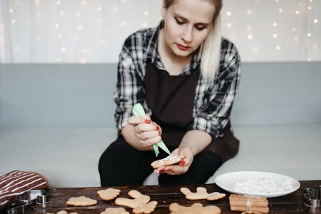 Icing of Christmas bakery. Woman decorating honey gingerbread cookies at home kitchen. Christmas and...