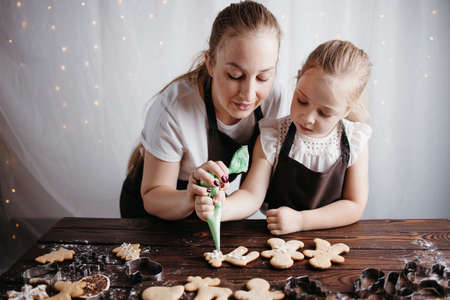 Christmas and New Year celebration traditions. Family home bakery, cooking traditional festive sweets. Mother and daughter decorating Christmas gingerbread cookies with icingの写真素材