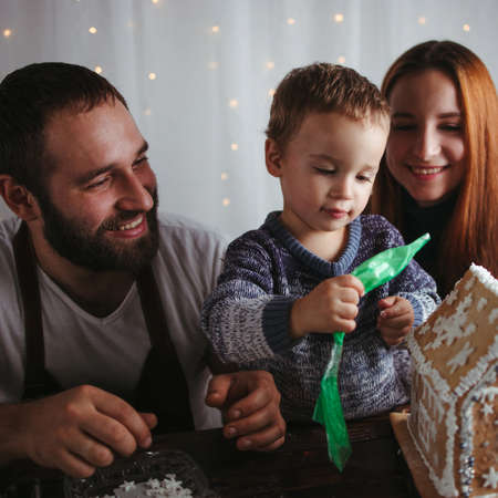 Family values, happy parents, Christmas time. Mother, father and son decorating Christmas gingerbread houseの写真素材