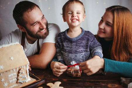 Family values, happy parents, Christmas time. Mother, father and son packing gingerbread cookies