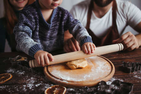 Christmas and New Year celebration. Family time. Holidays. Mother, father and son kneading gingerbread dough with rolling pin. Togethernessの写真素材