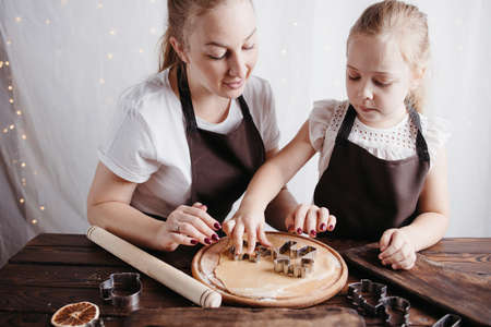 Family time, winter holidays tradition, cooking. Mother and daughter cutting cookies of raw gingerbread doughの写真素材