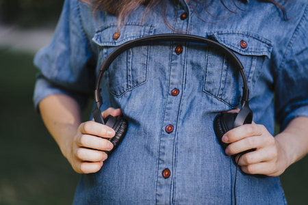 Beautiful pregnant woman holding headphones on her belly. Intrauterine growth, pregnancy, maternity,...