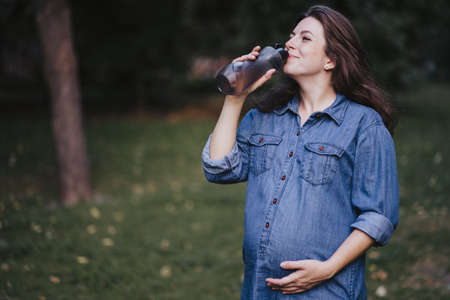 Pregnant woman drinking water during outdoor walk. Healthy pregnancy, active lifestyleの写真素材