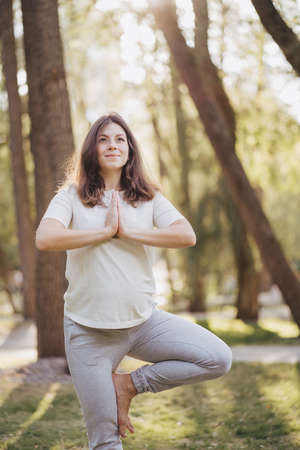 Pregnant woman doing yoga exercises on fitness mat outdoors at sunset. Healthy pregnancy, happy motherhood conceptの写真素材