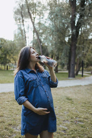 Pregnant woman drinking water during outdoor walk. Healthy pregnancy, active lifestyleの写真素材
