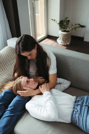Two young female friends embracing in living roomの写真素材