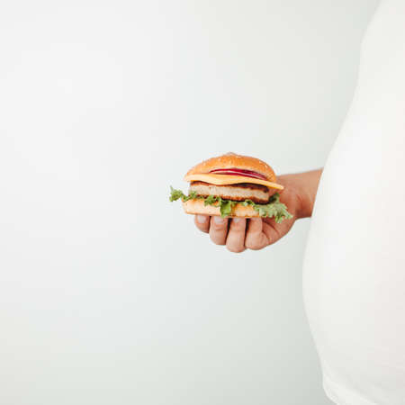 Fast food. Weight loss, diet, unhealthy eating, overeating. Overweight man with hamburger copy spaceの写真素材