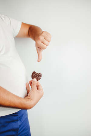 Obesity prevention, healthy lifestyle, diet. fattening food, high-calorie snack. Overweight man with unhealthy sweet cookie and thumb downの写真素材