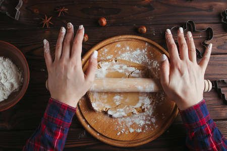 Christmas and New Year celebration traditions. Family home bakery, cooking traditional festive sweets. Woman rolling gingerbread dough with rolling pin on pastry boardの写真素材