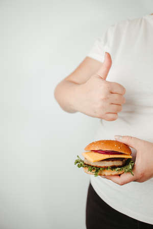 Balanced ration, diet, counting calories. Fast food and unhealthy snacks. Low calorie meals. Overweight woman with burger and thumb upの写真素材