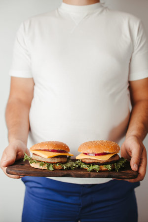 Fast food. Overeating. Weight loss diet, unhealthy eating. Overweight man with double portion of...