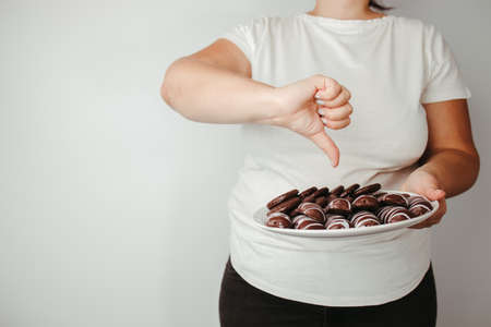 Weight loss, overweight, diet, unhealthy eating. Fat woman with plate of chocolate cookies and thumb downの写真素材