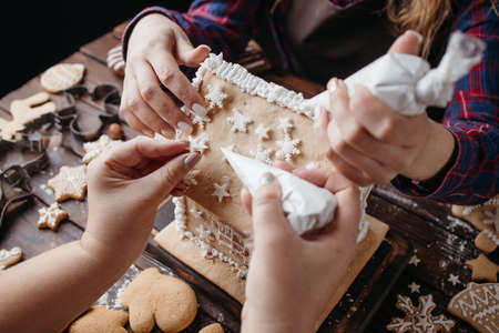 Christmas and New Year celebration traditions, festive sweets, family culinary. Traditional gingerbread. Friends decorating gingerbread house with icing and masticの写真素材