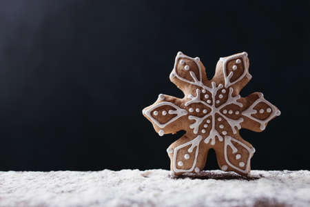 Christmas and New Year traditional attribute, festive sweets for kids, celebration mood. Homemade gingerbread snowflake cookie on dark backgroundの写真素材