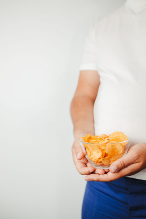 Overweight man eating fattening potato chips