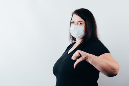 Dislike gesture. Covid-19. Lockdown quarantine. Ban. Bad choice. Young woman in medical mask showing...