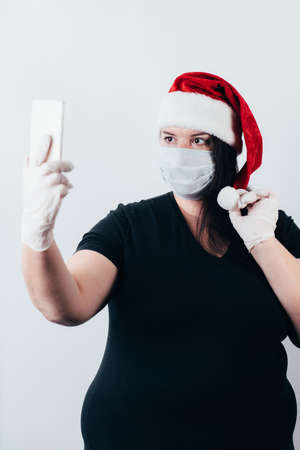 Christmas in corona crisis time. Woman wearing a face mask and gloves posting selfie in social media. Social distancing and online communicationの写真素材