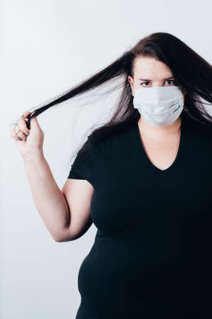 Hair care during the coronavirus pandemic. Brunette woman in medical mask touching her hairの写真素材