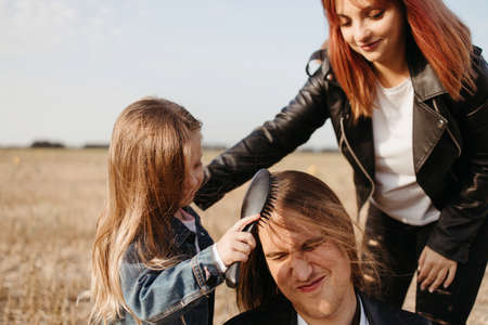 Family values, bonding, togetherness. Modern family. Mother and daughter braiding father's long hairの写真素材