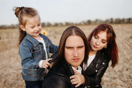 Family values, bonding, togetherness. Modern family. Mother and daughter braiding father's long hairの写真素材