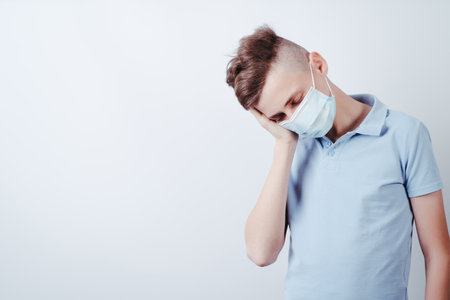 Stress, disturbing symptom, infection. Worried, desperate, frustrated boy in medical mask suffering from headache and pain. Concern, disquiet.の写真素材