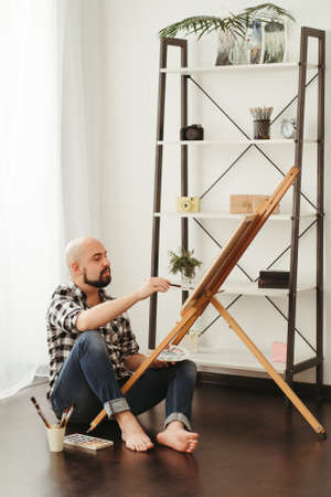 Fine art school. Homeschooling. Creative hobby. Young man doing watercolor painting at home studioの写真素材