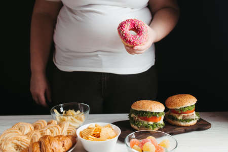 Unhealthy snack, junk food, compulsive overeating. Young overweight woman fighting the temptation to eat junk foodの写真素材