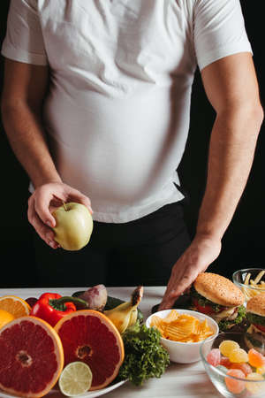Healthy snacking, balanced nutrition, dietary, lifestyle, weight loss concept. Overweight man choosing vegetables and fruits refusing junk foodの写真素材