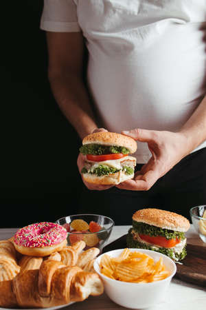 Food addiction, cheat meal, diet breakdown, compulsive overeating concept. Young overweight man fighting the temptation to eat junk foodの写真素材