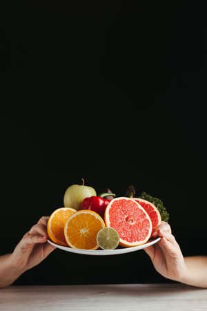 Diet, healthy lifestyle, weight loss, eating habits concept. Hands holding plate with fresh appetizing fruits and vegetablesの写真素材