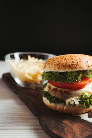 Close-up home made hamburger with cutlet, melted american cheese and french fries on wooden plate