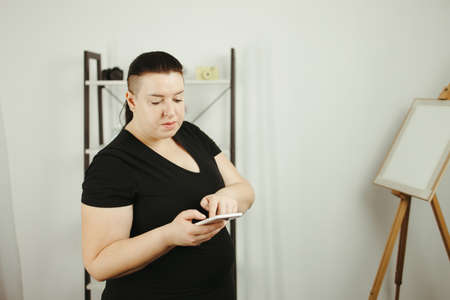 Fitness app, sport gadget, outdoor workout and technology. Overweight woman with smart phone in her living roomの写真素材