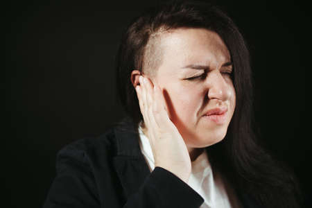 Young woman have headache migraine. Girl with earache is holding aching ear, nasty sound, body pain conceptの写真素材