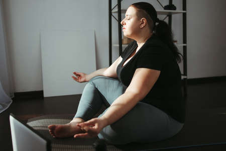 Overweight woman meditating in her living roomの写真素材