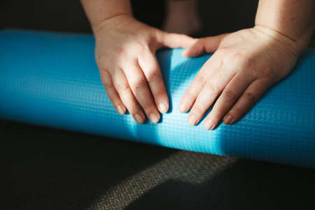 Hands of young woman rolling yoga mat, close upの写真素材