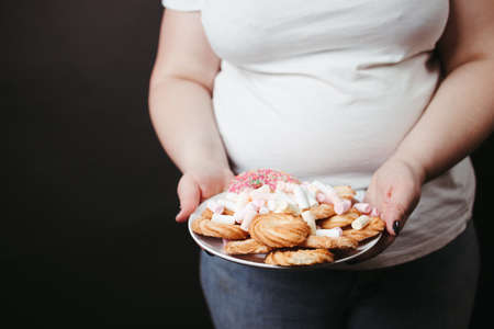 Overweight woman holding plate with tasty sweetsの写真素材