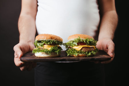 Overeating. Overweight man with two big hamburgers