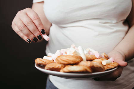 Overweight woman holding plate with tasty sweetsの写真素材