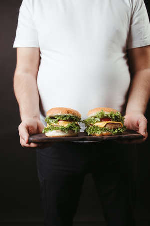 Obese man with two tasty fattening hamburgersの写真素材