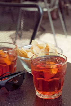 At the bar: two glasses with long drinks with oranges and potato chips on the tableの写真素材