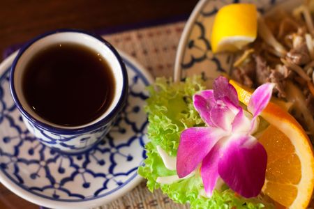 Lunch in a thai restaurant: thai noodles served beautifully with an otchid flower and a cup of tea, focus on the flowerの写真素材