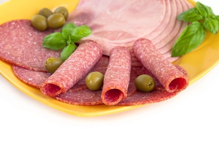 Sliced ham and sausage served on a plate with olives and fresh basilの写真素材