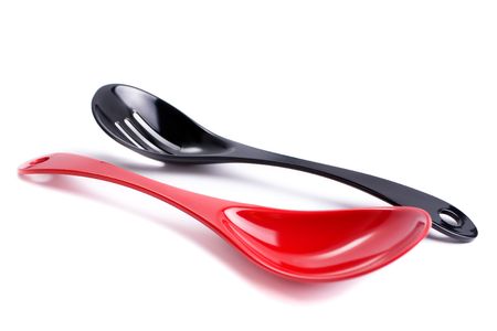 Two plastic kitchen utensils: red cooking spoon and black slotted spoon, isolated on whiteの写真素材