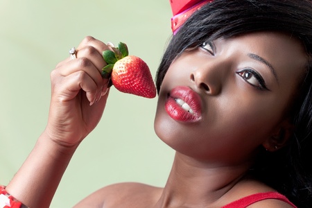 Beautiful young black woman eating a strawberry, closeup shotの写真素材