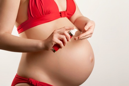 Skin care in pregnancy concept  young pregnant woman applying body cream, closeup shotの写真素材
