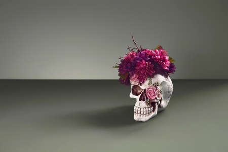 Day of The Dead skull adorned with purple flowers. On pastel dark green background with copy spaceの写真素材
