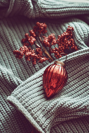Red Christmas decorations on blue woven sweater, minimalistic color scheme, lots of texture.