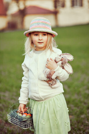 Little girl collecting dyed eggs on Easter egg hunt, on country farm, outdoor