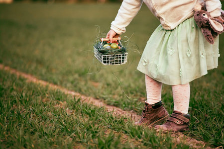Cute caucasian pre-schooler blonde girl at Easter egg hunt by grandmas country house, outdoor